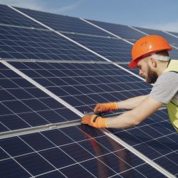 Male worker with solar batteries. Man in a protective helmet. Installing stand-alone solar panel system.